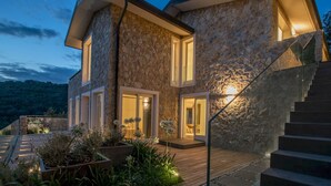 Une maison moderne en pierre, dotée d’une terrasse en bois, d’un escalier et d’une entrée bien éclairée.