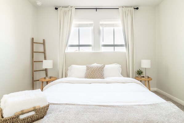 Une chambre à coucher avec un lit, deux tables de chevet, une échelle en bois, une fenêtre avec des rideaux et une petite plante posée sur l’une des tables.