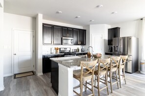 Une cuisine moderne avec des meubles de couleur sombre, des appareils en acier inoxydable et un îlot central doté de tabourets de bar.