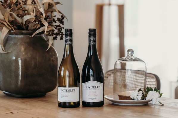 Two wine bottles, a glass dome, and a plate with a dessert on a wooden table.