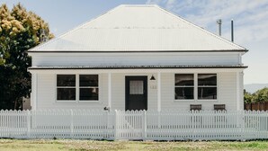 A white two-story house with a picket fence, a black front door, and a chimney. - Luxe Historic River Port Stay - Pay 2, Stay 3* (Morpeth)