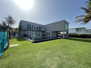 Une maison moderne à deux étages, dotée d’une piscine, d’un patio couvert et d’une pelouse bien entretenue.