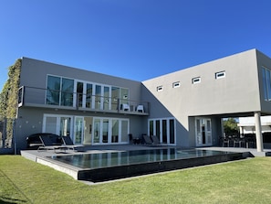 Une maison moderne à deux étages, dotée d’une piscine, de grandes fenêtres et d’un balcon.