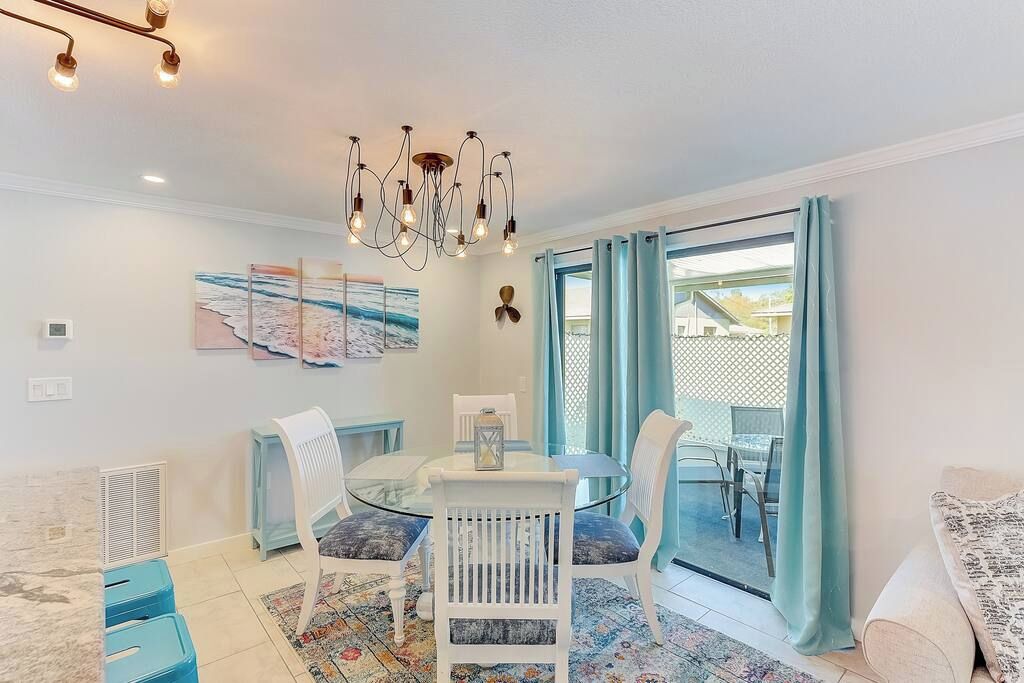 A dining area with a glass table and chairs, a chandelier, and a view through a glass door.