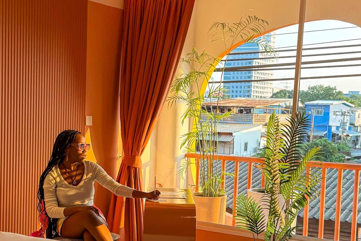 A balcony with a view of a cityscape, a potted plant, and a person sitting by the window.