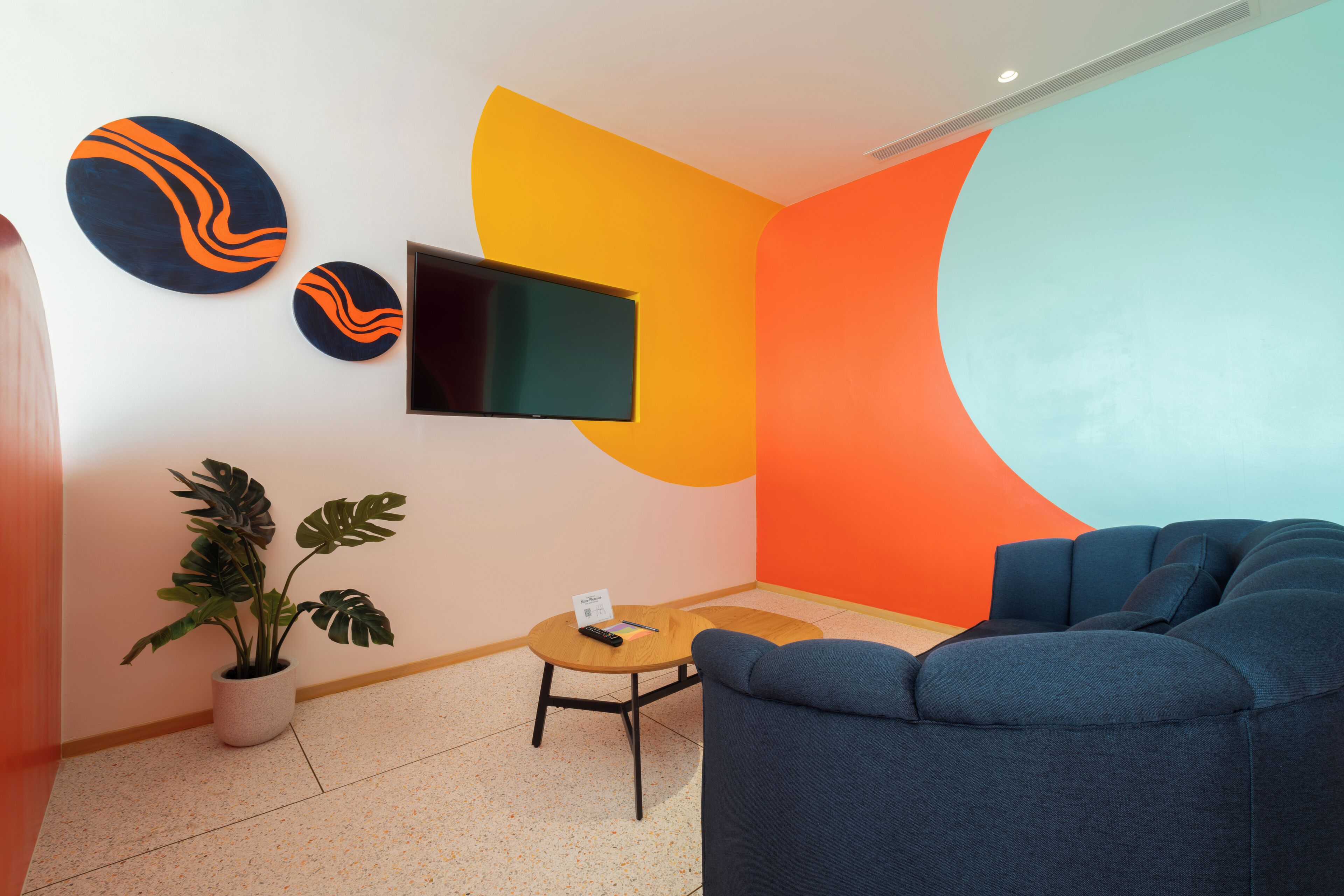 A modern living room with a blue sofa, a flat-screen TV, abstract wall art, and a potted plant.
