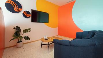 A modern living room with a blue sofa, a flat-screen TV, abstract wall art, and a potted plant.