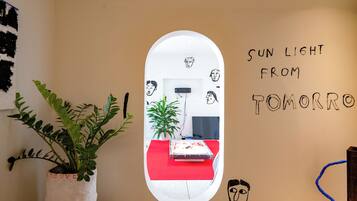A room with a white wall, a mirror reflecting a red sofa and a plant, and a wall with text 'SUN LIGHT FROM TOMORROW'.