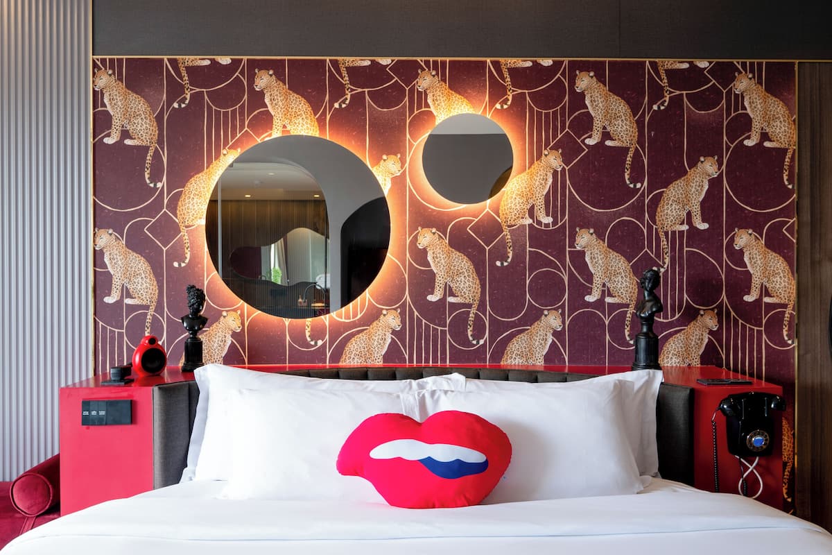 A hotel room with a large bed, a red telephone, and a wall with leopard patterns.