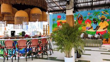 A restaurant with a tropical mural, wicker hanging lamps, and a potted plant.