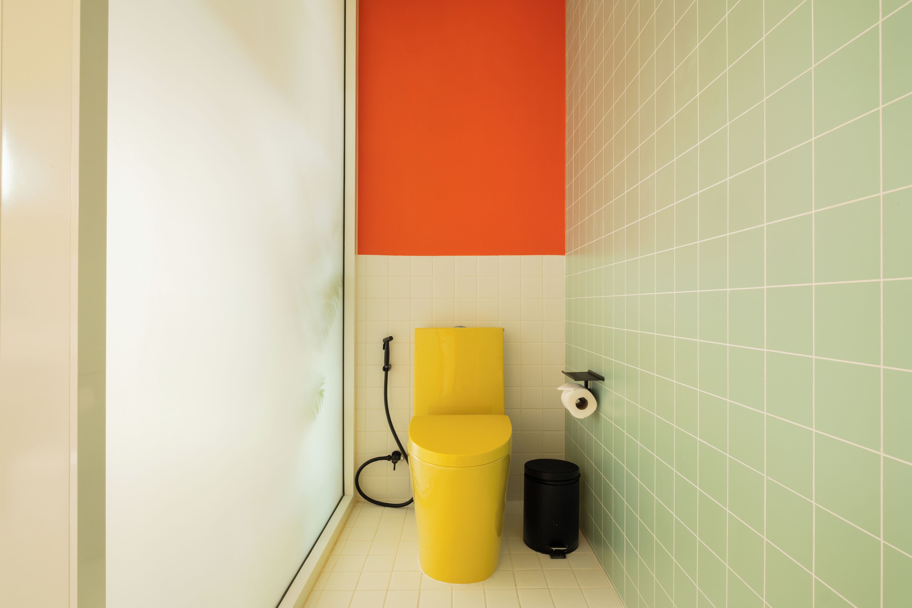 A bathroom with a yellow toilet, a black trash bin, and a green tiled wall.