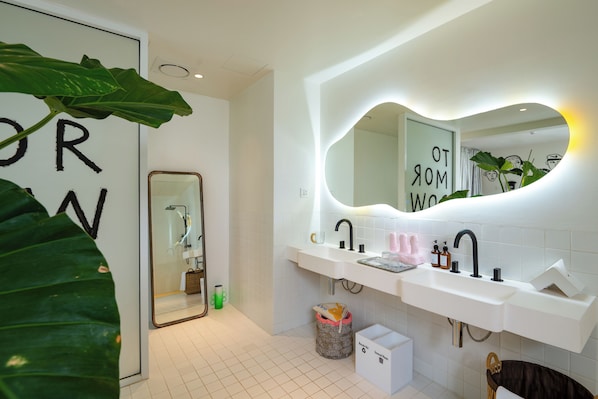 A modern bathroom with a white sink, a large mirror, and a plant. - The Fig Lobby Bangkok (Bangkok)