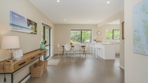 A modern kitchen with a dining area, large windows, and a view of the outdoors. - Seas the Day - Matarangi Holiday Home (Matarangi)