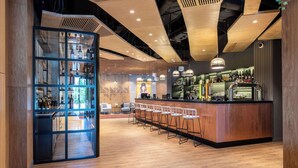 A modern bar area with a wooden bar counter, multiple stools, and a glass display case with bottles. - Sadu Hotel Almaty, a member of Radisson Individuals (Almaty)