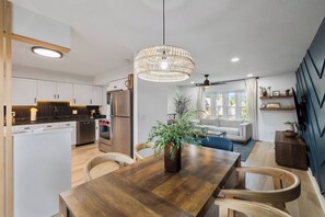 Una cocina moderna con armarios blancos, una mesa de comedor de madera y una lámpara colgante.