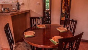 A round wooden dining table with four chairs, a kitchen counter with utensils, and a decorative mirror. - Oilepo Cottage (Naivasha)