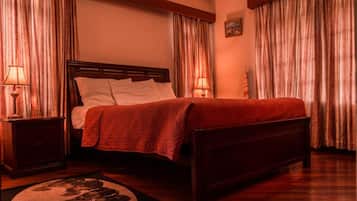 Ein ordentlich bezogenes Bett mit roter Decke, zwei Nachttische mit Lampen und ein Blumenmuster-Teppich auf dem Boden.