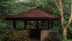 A gazebo with a stone base and a wooden roof, surrounded by lush greenery and flowering bushes. - Oilepo Cottage (Naivasha)