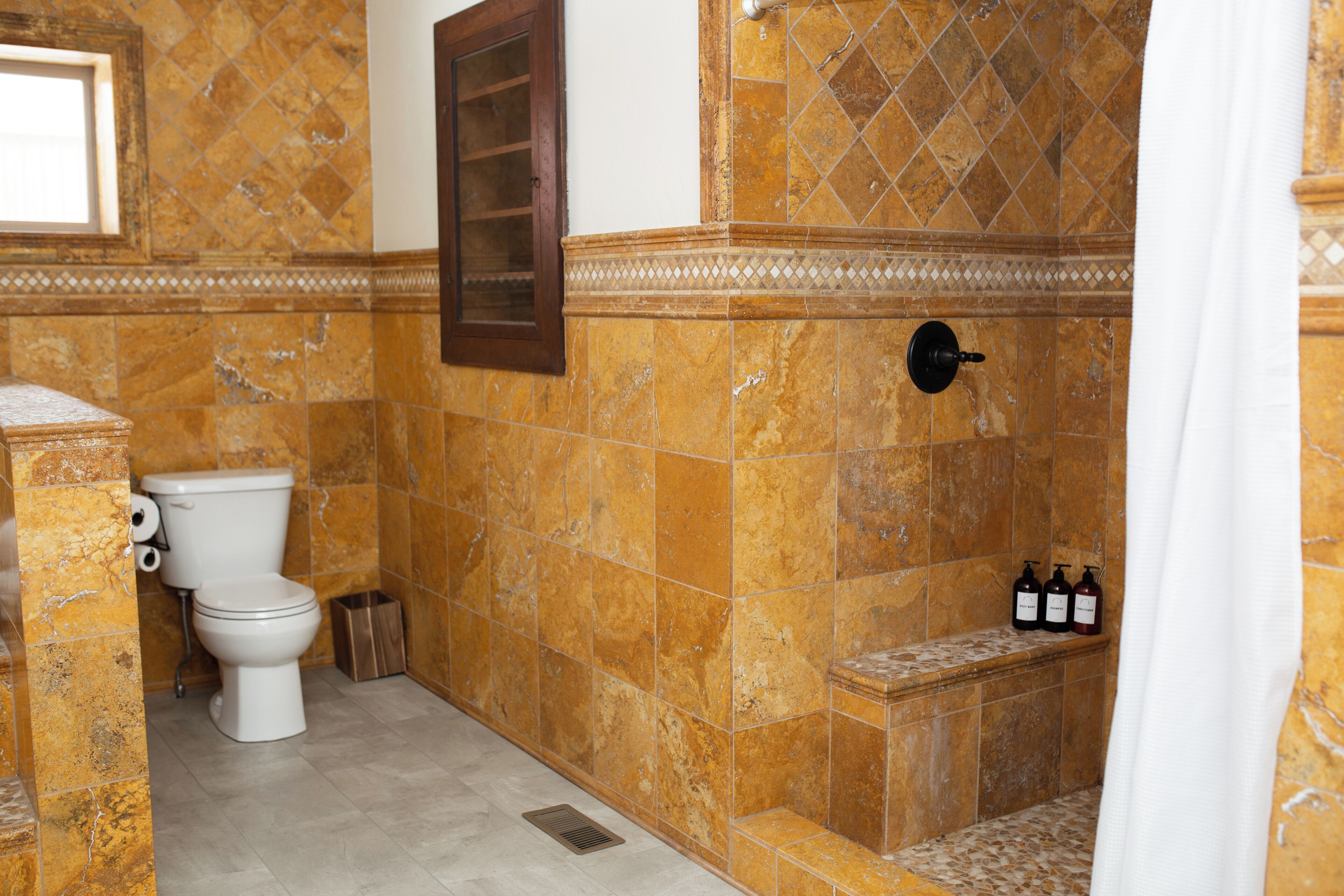 A bathroom with a toilet, shower, and a shelf with toiletries.