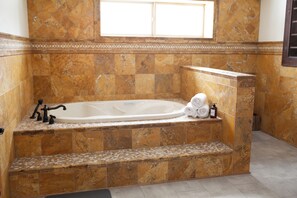 Un baño con una bañera grande, paredes de mármol y un ventanal superior.