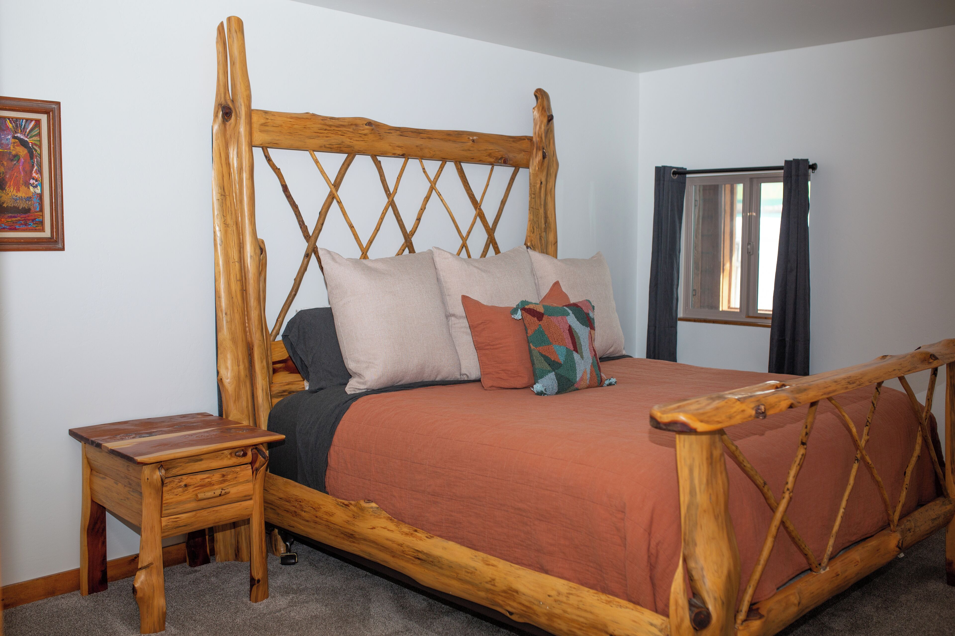 Een houten bed met hoofdbord, een nachtkastje en een raam met gordijnen.