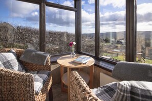 A cozy seating area with wicker furniture and a small wooden table, a book, and a vase with flowers.