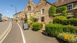 A historic stone building with a church tower, a signboard for 'The Sandpiper Restaurant', and a well-maintained garden with hedges and flowers. - Oak Lodge House, Leyburn, Yorkshire Dales (Leyburn)