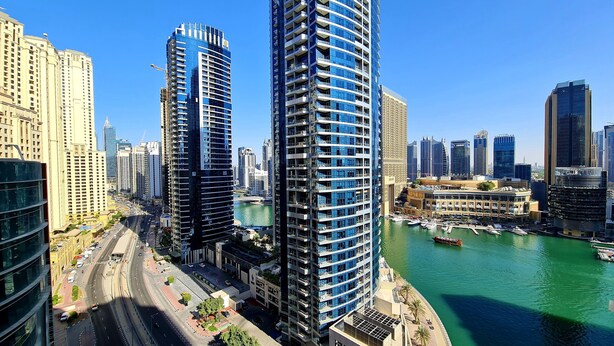 A high-rise building with a modern architectural design, situated next to a body of water with boats docked. - Marco Polo - Stunning Marina Views | High Floor | Close to Tram (Dubai)