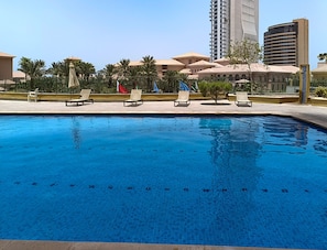 A swimming pool with lounge chairs and palm trees, surrounded by buildings.