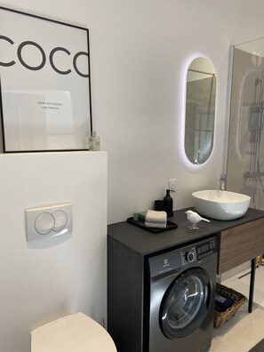 Un baño moderno con un espejo grande, un lavabo, una lavadora y un inodoro.