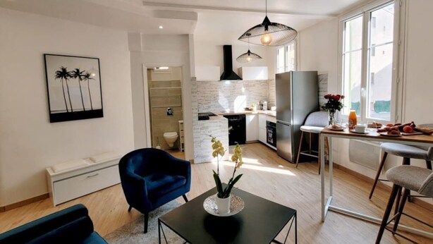 A modern kitchen with a large island, a dining area with a bar stool, and a living room with a blue chair. - Ze Perfect Place - Comfortable 2 Bedroom Apartment - Asc - Port - Garibaldi (Nice)
