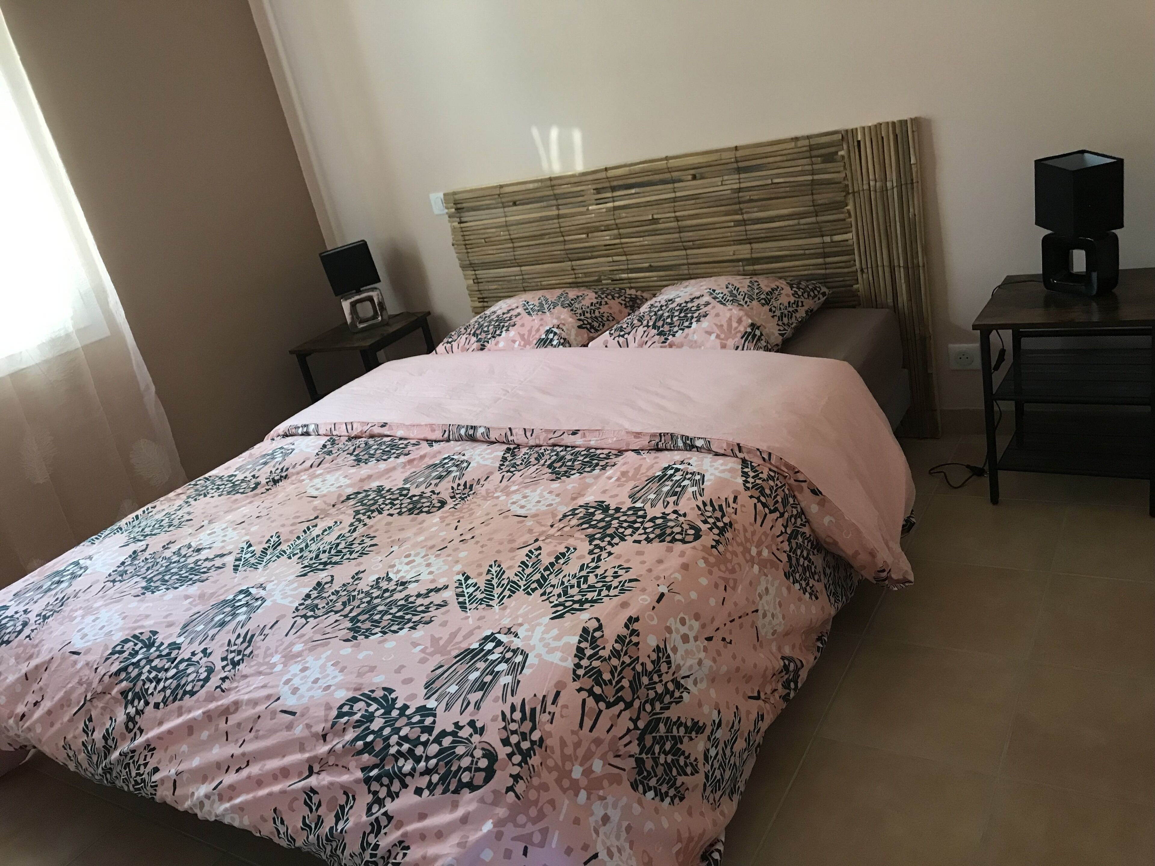 A neatly made bed with a patterned bedspread, a bedside table with a lamp, and a wall-mounted light fixture.