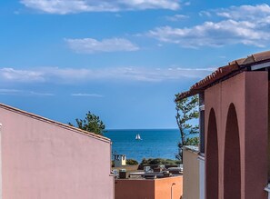 Une vue sur la côte, avec un voilier sur l'eau, des bâtiments au premier plan et un ciel dégagé.