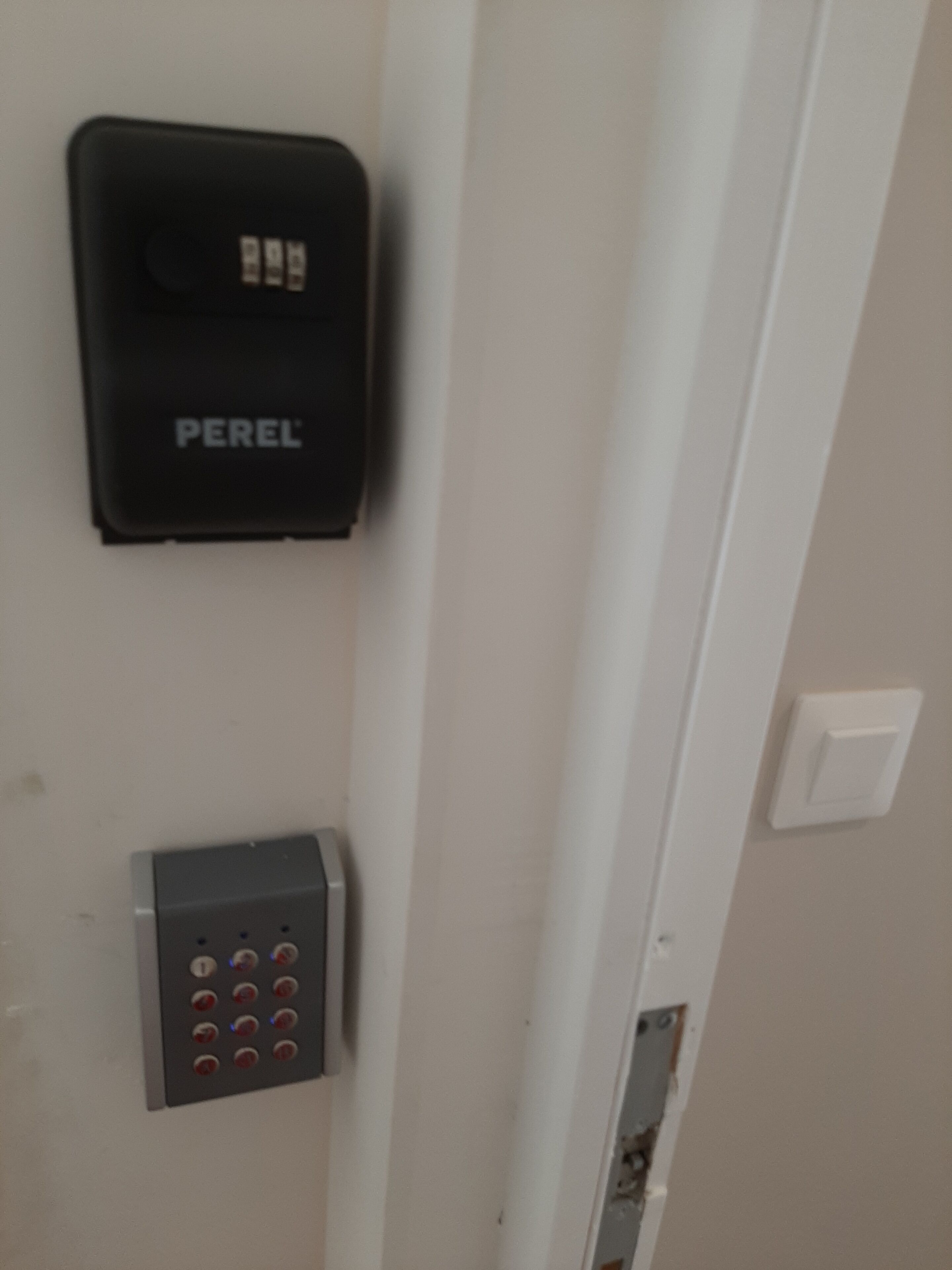 A door with a black security device labeled "PEREL" and a keypad with red buttons.