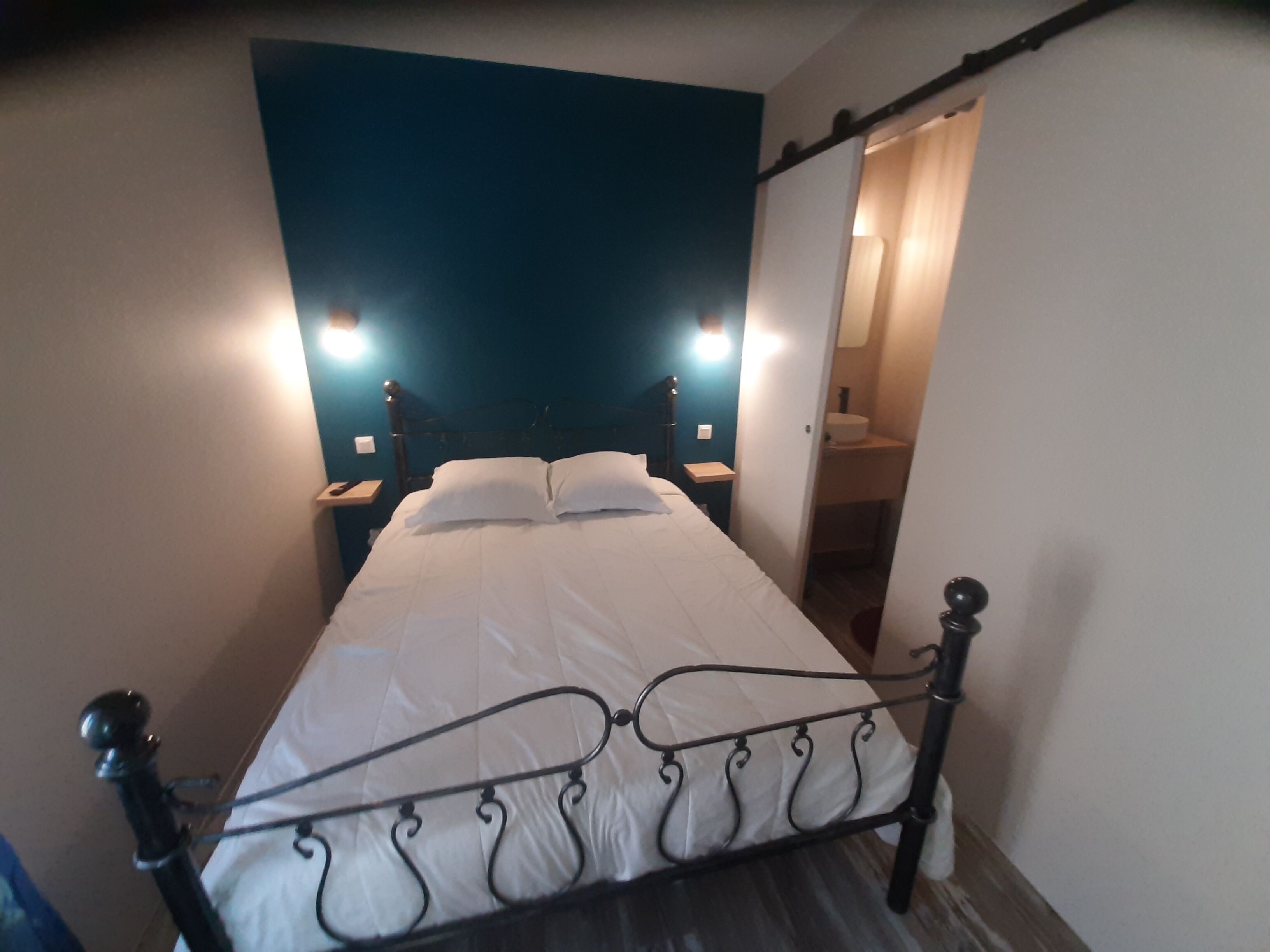 Una cama bien hecha con sábanas blancas, cabecera de metal y dos lámparas de noche.