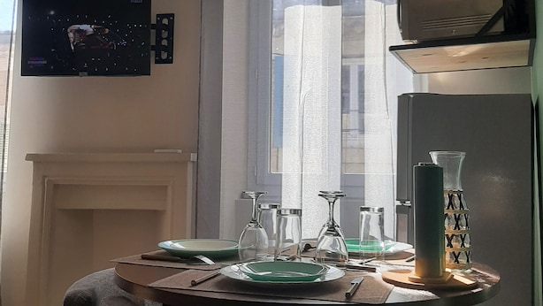 Un comedor con una mesa preparada para dos personas, un televisor montado en la pared y una ventana con cortinas.