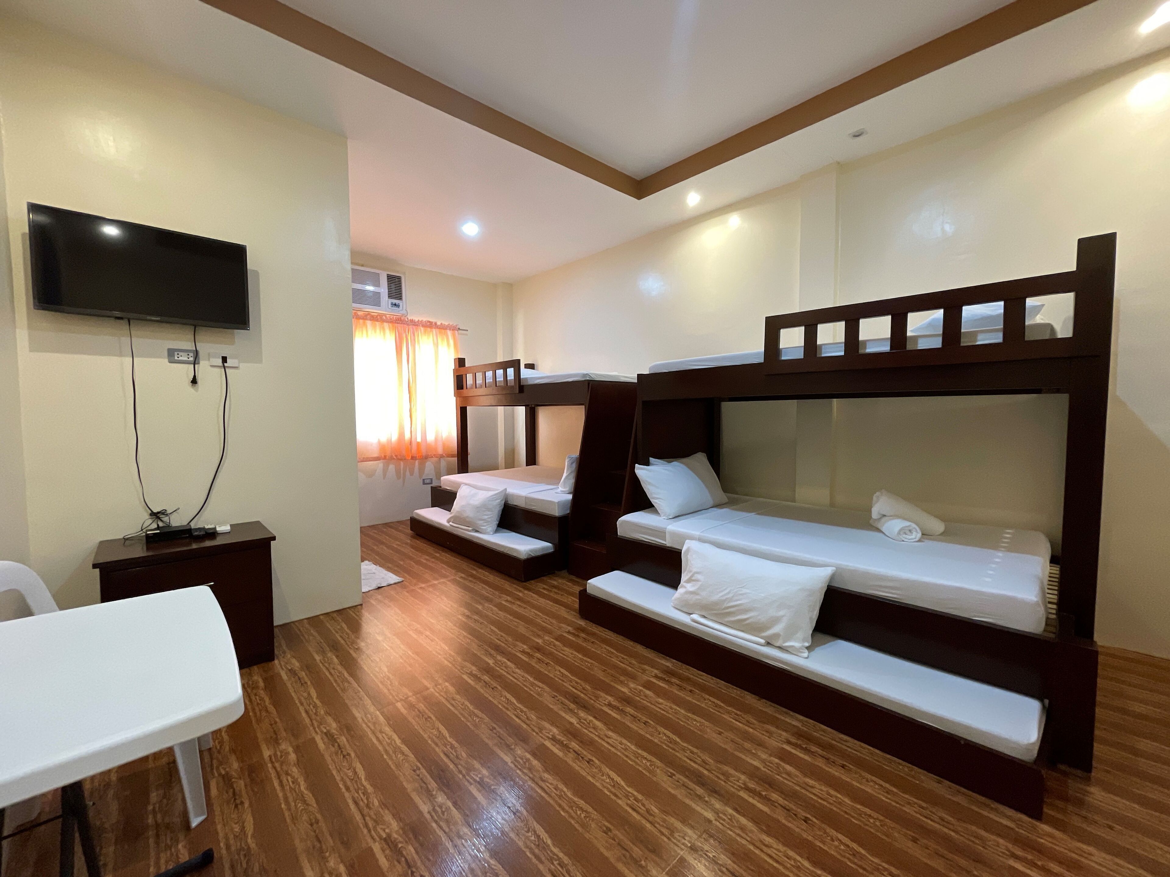 A hotel room with bunk beds, a flat-screen TV mounted on the wall, a desk, and a window with curtains.