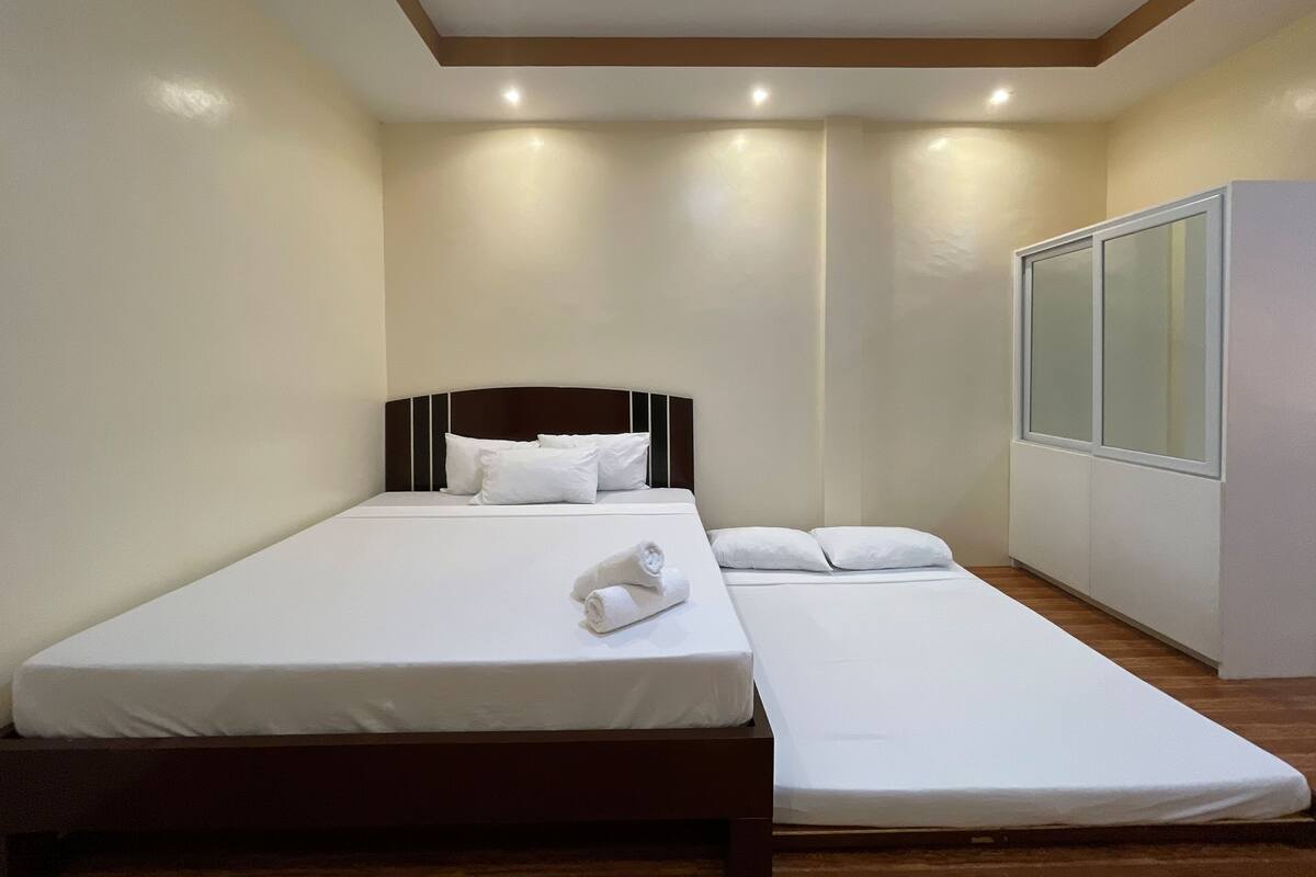 Une chambre d’hôtel avec un lit simple, un petit canapé, une armoire et une grande fenêtre.