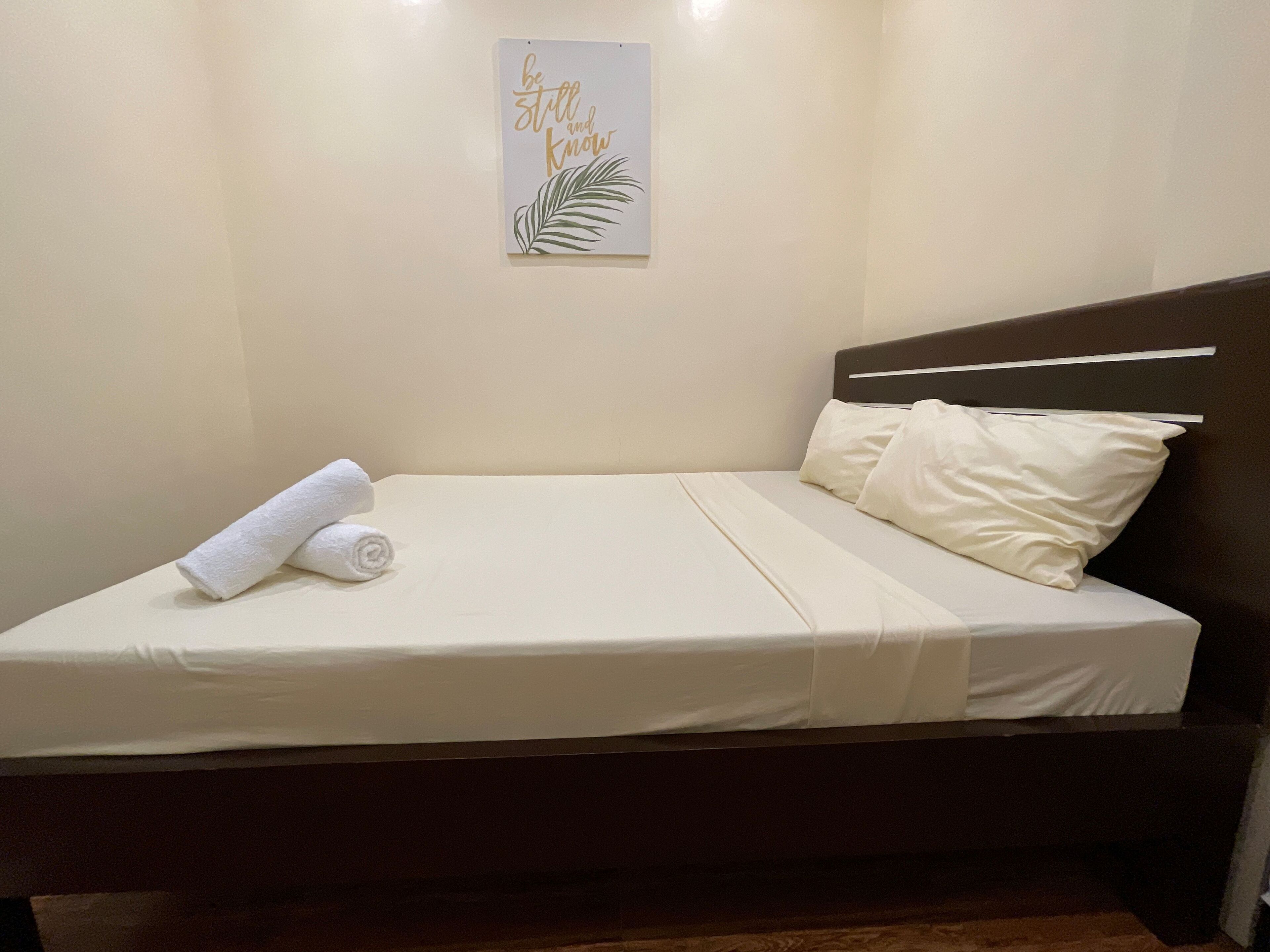 A neatly made bed with white linens, a rolled towel, and a single pillow.