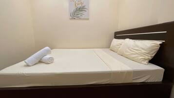 A neatly made bed with white linens, a rolled towel, and a single pillow.