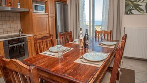 Une cuisine dotée de meubles en bois, d’un four à micro-ondes, d’un réfrigérateur et d’une table à manger mise pour six personnes, avec assiettes, verres et une bouteille.