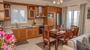 Une cuisine bien éclairée, avec des meubles de rangement en bois, une table à manger dressée pour quatre personnes et une vue sur l’extérieur par la fenêtre.