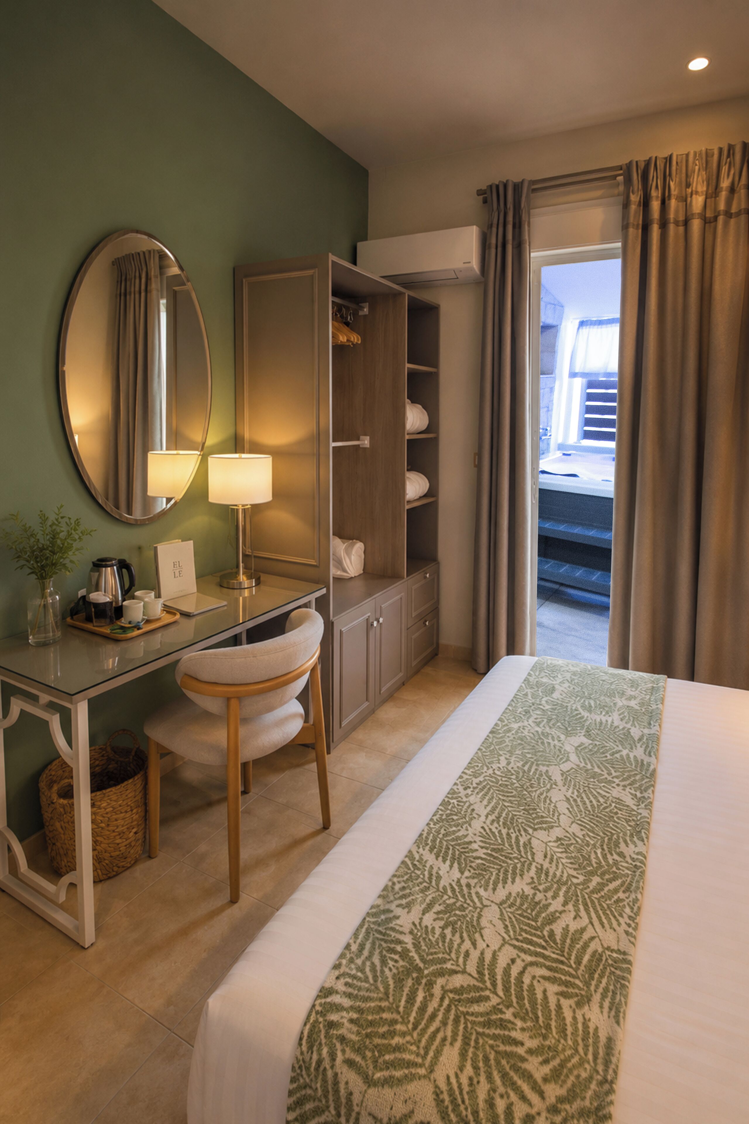 A hotel room with a bed, a desk with a lamp, a wardrobe, a mirror, and a view through the window.