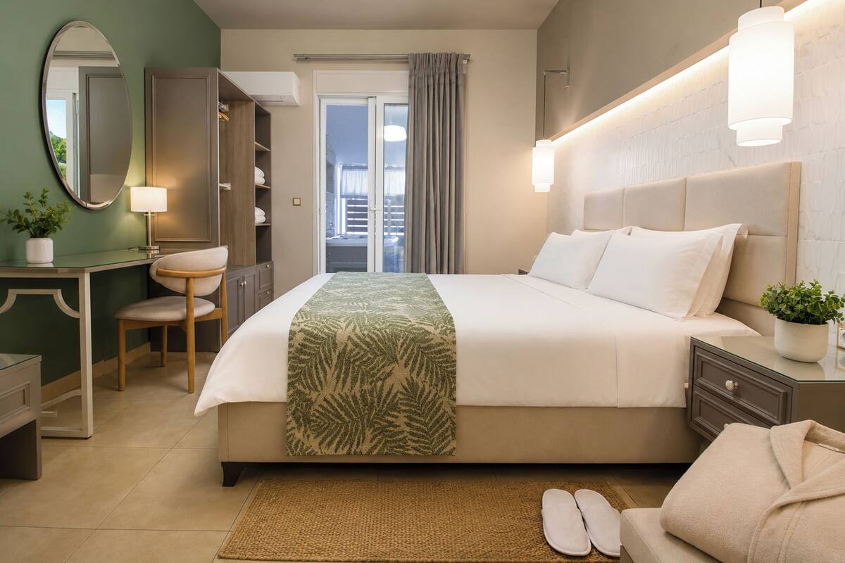 A hotel room with a bed, bedside table, lamp, chair, and a view of the outside.