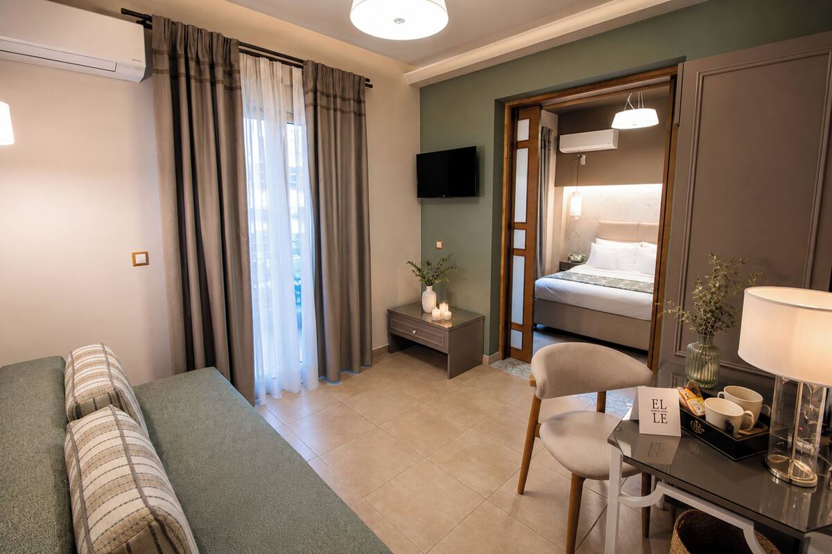 A hotel room with a bed, a desk with a lamp, a chair, a TV, and a window with curtains.