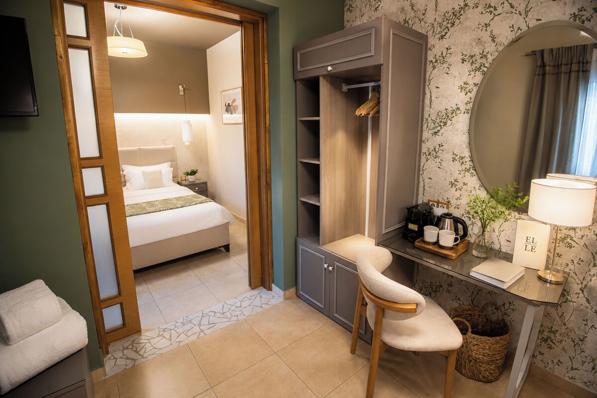 A hotel room with a bed, a desk with a chair, a mirror, and a small table with a lamp.