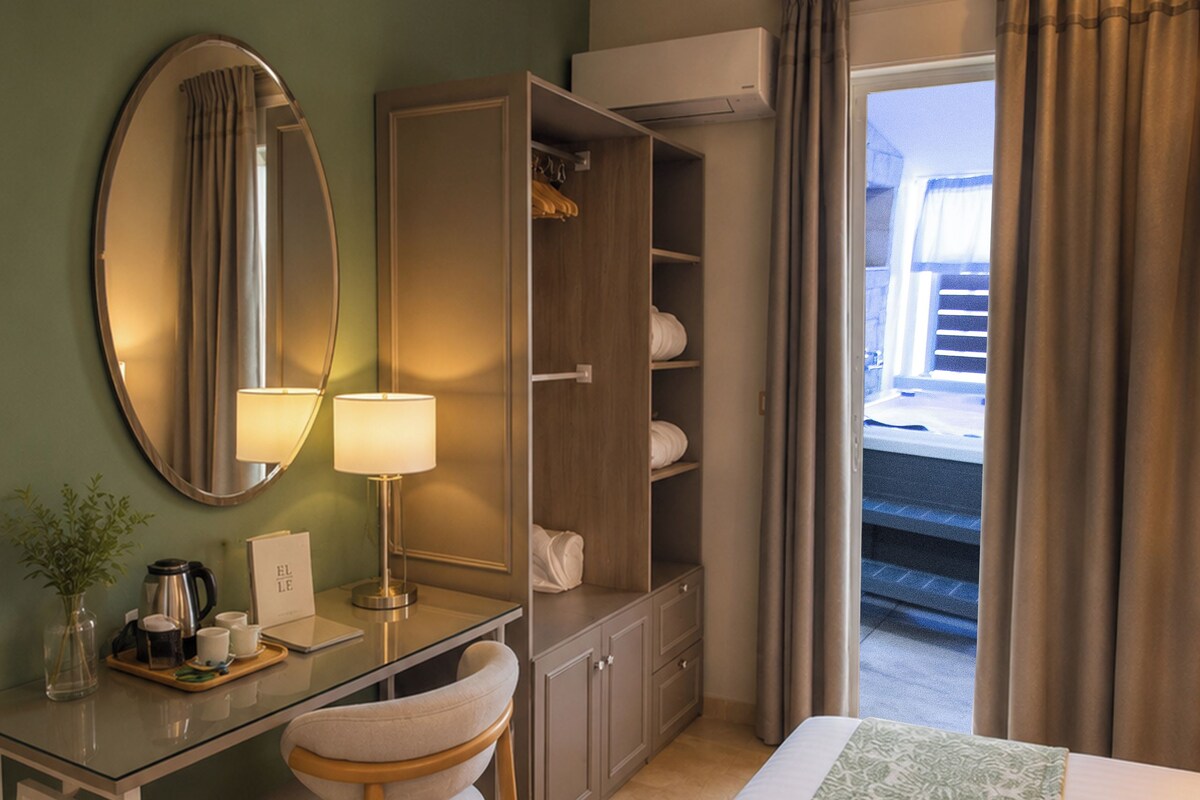 A hotel room with a bed, a desk with a lamp, a wardrobe, a mirror, and a view through the window.