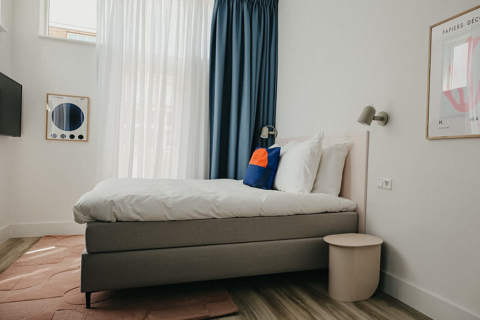 Quarto moderno com uma cama-sofá cinza, uma mesinha de cabeceira, uma luminária e um quadro na parede.