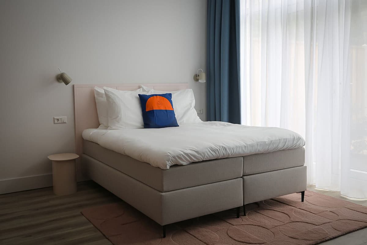 Ein modernes Schlafzimmer mit einem Bett, einem kleinen Nachttisch und einem Fenster mit Vorhängen.