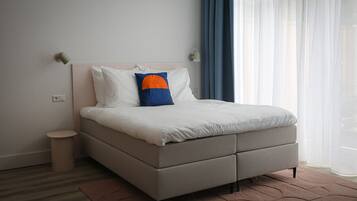 A modern bedroom with a bed, a small bedside table, and a window with curtains.